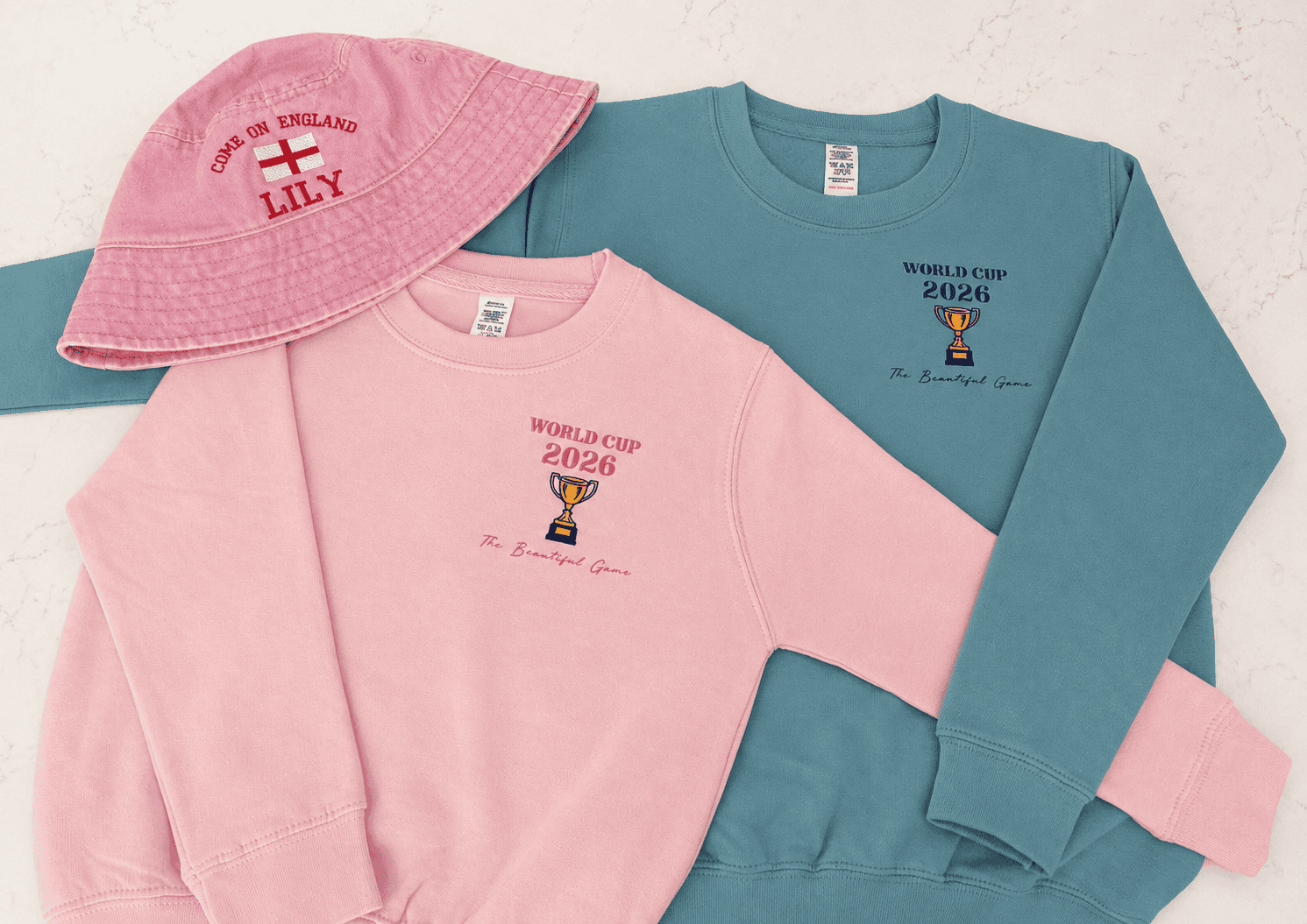 Customised pink and blue sweatshirts with World Cup 2026 logo and matching cap for sports fans.
